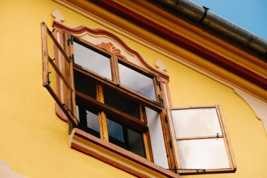 Parlak, güneşli, sarı bir duvara dayanan büyüleyici bir ahşap pencereyi gösteren güzel bir resim.