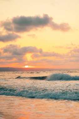 Güzel, sakin bir gün batımı okyanus dalgalarını aydınlatıyor. Huzurlu ve huzurlu bir sahil atmosferi yaratıyor.