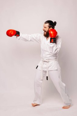 Beyaz kimonolu bir dövüş sanatları ustası kırmızı boks eldivenleriyle yumruk atıyor, bağlılığını ve disiplinini gösteriyor.