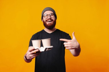Gözlüklü ve bereli mutlu bir adam, parlak sarı arka planda aynı kahve fincanlarını sergiliyor.