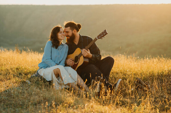 A loving couple enjoys music in a picturesque field at sunset, creating a serene and memorable atmosphere