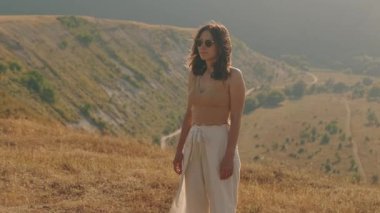 Bir kadın zarif ve manzaralı doğal bir manzarada duruyor, hem sükuneti hem de tarzı somutlaştırıyor.