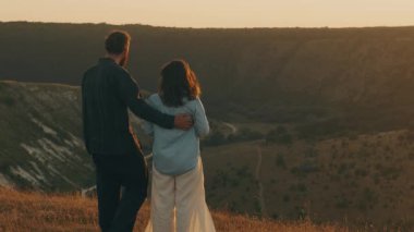 Bir çift, güzel bir gün batımında nefes kesici manzaraya bakan hassas ve samimi bir anı paylaşır.