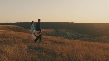Romantik bir sahnede, gün batımında altın çayırlarda el ele yürüyen bir çift gitar tıngırdatıyor.
