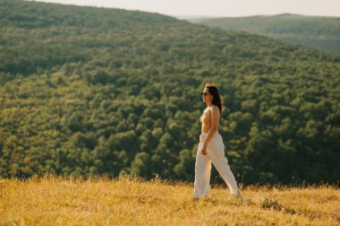 Bir kadın bugün güneşli bir gökyüzünün altında yemyeşil doğada güzel ve huzurlu bir yürüyüşün tadını çıkarıyor.