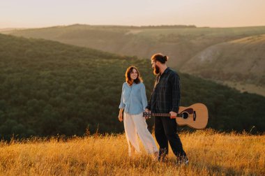 Sevgi dolu bir çift, açık havada romantik bir anın tadını çıkarır. Nefes kesici bir gün batımında güzel bir gitarla dolaşırlar.
