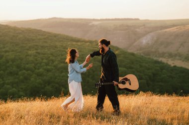 Neşeli bir çift, resim gibi bir günbatımı manzarasında birlikte mutlu bir şekilde dans eder.