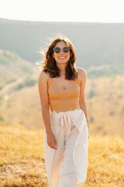 Şık güneş gözlüğü takan neşeli genç bir kadın çarpıcı bir açık hava manzarasına karşı mutlulukla parıldıyor.