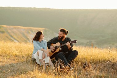Sevgi dolu bir çift, canlı ve güneşli bir manzarada akustik gitar çalarak güzel bir romantik anın tadını çıkarır.
