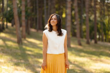 Güneşli bir ormanda doğanın güzelliğinin tadını çıkaran huzurlu ve huzurlu bir kadın portresi.