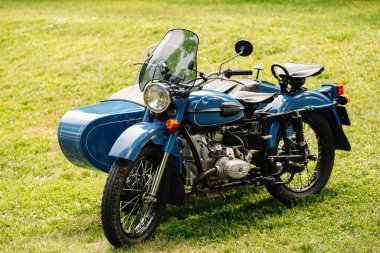 Klasik bir cazibe ve karizma yayarak yemyeşil bir alana park edilmiş, sepetli klasik mavi bir motosiklet.