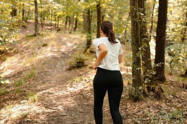 Genç bir kadın neşe içinde güzel, sakin bir orman yolunda koşuyor, doğanın güzelliğine dalmış.