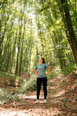 Bir kadın, canlı yeşil ormanda güven içinde duruyor ve doğanın huzurunun tadını çıkarıyor.