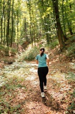 Huzurlu bir kadın, canlı ağaçlar ve çarpıcı doğal güzelliklerle çevrili sakin bir ormanda koşmaktan zevk alır.