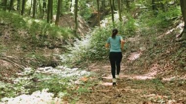 Bir kadın, canlı yeşilliklerle çevrili güzel manzaralı ve resimli bir orman yolunda hızla koşar.