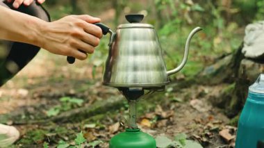 Bir insan doğada taşınabilir bir ocakta paslanmaz çelik bir çaydanlık hazırlar. Açık hava maceraları için birebirdir..
