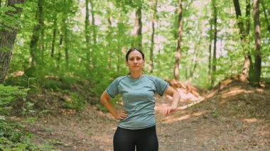 Canlı bir orman ortamında esneme egzersizleri yapan bir kadın, zindelik ve sağlığını gösteriyor..