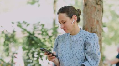 Kablosuz kulaklık takarken akıllı telefonunu kullanan bir kadın doğal ortamının tadını çıkarıyor.