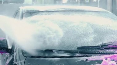Dinamik bir araba yıkama sahnesi canlı bir şekilde hareket halindeki bir araca köpük ve su spreyi sıçratıyor.