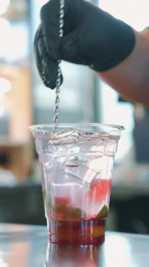 Yetenekli bir barmen, şeffaf bir bardakta lezzetli ve ferahlatıcı bir içeceği buz ve nane ile ustalıkla karıştırır.