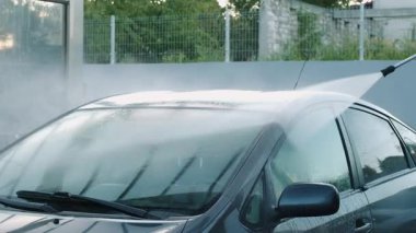 Yüksek basınçlı spreyle yıkanan bir arabanın görüntüsü, iş başındayken temizliği gösteriyor..