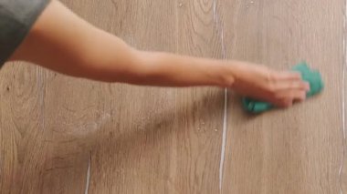 Bir insan yeşil bir bezle ahşap bir yüzeyi özenle temizler. Böylece pırıl pırıl temiz bir son elde eder.