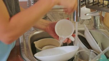 Güneşli bir mutfakta bulaşık yıkayan, temizlik sanatını sergileyen ve evi düzenli tutan biri..