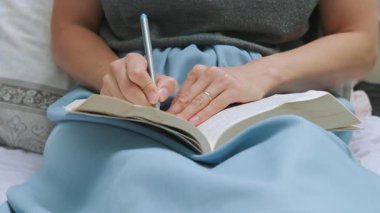 Bir insan yatağına oturur, rahat bir kitaba notlar yazar, odaklanma ve rahatlama ile dolu sıcak bir atmosfer yaratır.