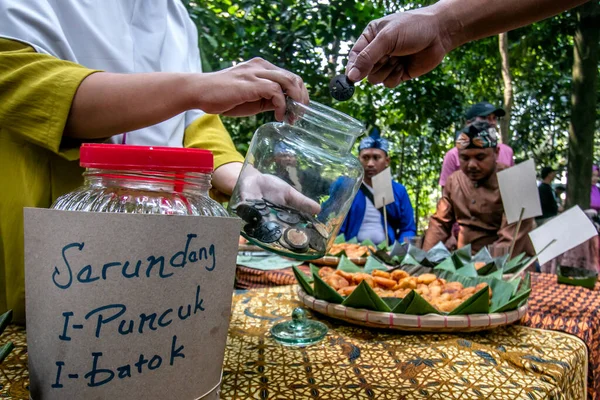 Bogor City, Endonezya - 23 Temmuz 2023 - Alıcılar bir köy çerez festivalinde para yerine bir kabuk değerinde hindistan cevizi kabuğu kırıntılı abur cuburlar için ödeme yapıyorlar.