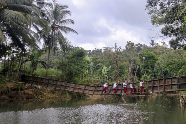 Sukabumi, Endonezya - 24 Temmuz 2024: Sukabumi, Batı Java, Endonezya 'daki Cikaso nehri üzerindeki hasarlı bir köprüde yürüyen öğrenciler, nehir şiddetli yağış nedeniyle köprü seviyesine ulaşınca iki köyü birbirine bağlayan köprü hasar gördü