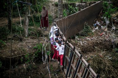 Sukabumi, Endonezya - 24 Temmuz 2024: Sukabumi, Batı Java, Endonezya 'daki Cikaso nehri üzerindeki hasarlı bir köprüde yürüyen öğrenciler, nehir şiddetli yağış nedeniyle köprü seviyesine ulaşınca iki köyü birbirine bağlayan köprü hasar gördü