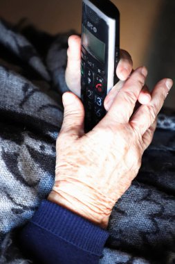 Telefonu ve uzaktan kumandası olan yaşlı bir kadın.