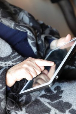 Oturma odasında tablet bilgisayar kullanan yaşlı kadın.