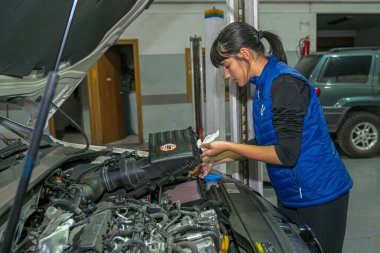 Genç bayan tamirci, bir araba motorunun tamiri üzerinde çalışıyor.