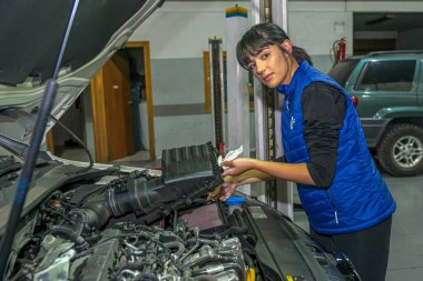 Genç bayan tamirci, bir araba motorunun tamiri üzerinde çalışıyor.