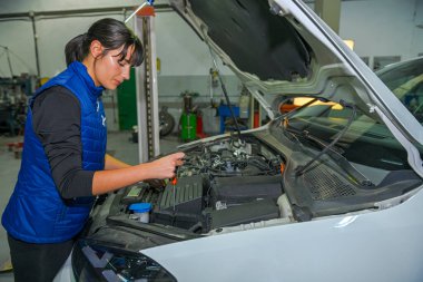 Genç bayan tamirci, bir araba motorunun tamiri üzerinde çalışıyor.
