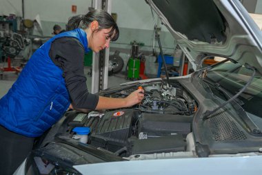 Genç bayan tamirci, bir araba motorunun tamiri üzerinde çalışıyor.