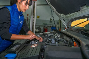 Genç bayan tamirci, bir araba motorunun tamiri üzerinde çalışıyor.