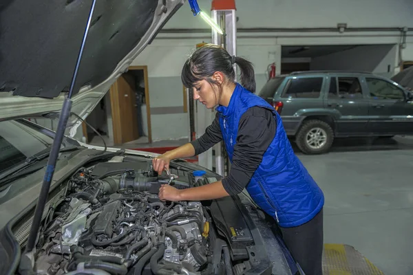 Genç bayan tamirci, bir araba motorunun tamiri üzerinde çalışıyor.