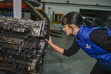 Genç bayan tamirci, bir araba motorunun tamiri üzerinde çalışıyor.