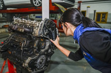 Genç bayan tamirci, bir araba motorunun tamiri üzerinde çalışıyor.