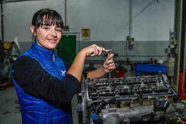 Genç bayan tamirci, bir araba motorunun tamiri üzerinde çalışıyor.