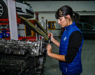 Genç bayan tamirci, bir araba motorunun tamiri üzerinde çalışıyor.
