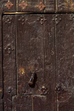 Dark wooden door adorned with iron studs and a vintage hand-shaped door knocker.