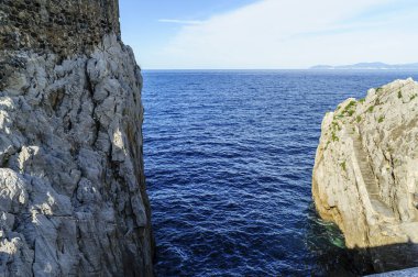 Doğal bir kireçtaşı uçurumu berrak gökyüzünün altındaki sakin mavi deniz sularının üzerinde görkemli kuleler.