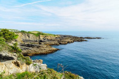 Kuzey İspanya 'nın engebeli kıyıları boyunca açık mavi gökyüzü boyunca çarpışan katmanlı kaya oluşumları..