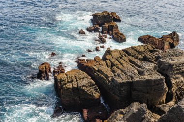 Kuzey İspanya 'nın engebeli kıyıları boyunca açık mavi gökyüzü boyunca çarpışan katmanlı kaya oluşumları..