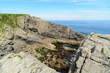 Kuzey İspanya 'nın engebeli kıyıları boyunca açık mavi gökyüzü boyunca çarpışan katmanlı kaya oluşumları..