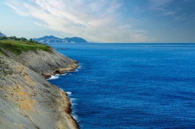 Kuzey İspanya 'nın engebeli kıyıları boyunca açık mavi gökyüzü boyunca çarpışan katmanlı kaya oluşumları..