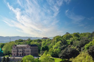 Comillas, Cantabria, İspanya 'nın bereketli manzarasında gündüz vakti aya karşı kurulmuş görkemli tarihi bir konak.
